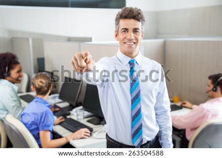 Portrait of male manager pointing at you while customer service executives working in background at call center