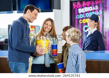 Happy family of four having snacks while female worker standing at cinema concession stand