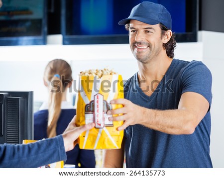 Happy male seller selling popcorn to man at cinema concession stand with colleague in background