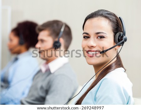 Portrait of smiling female customer service representative with colleagues in background at office