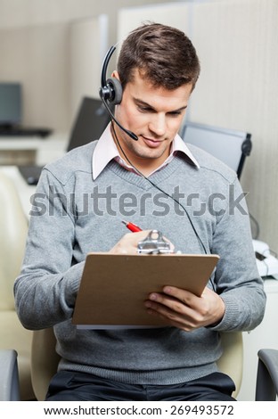Young male customer service representative writing on notepad in office