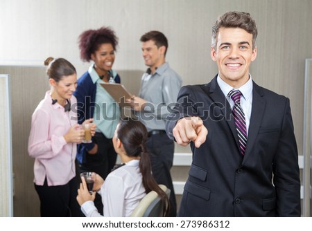 Portrait of smiling manager pointing at you while employees working in background at call center
