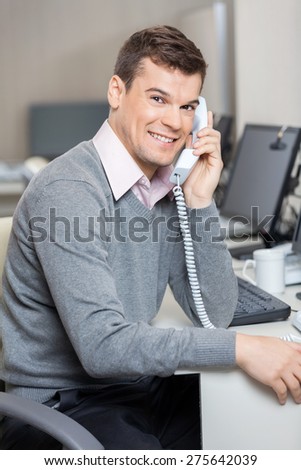 Portrait of young male customer service representative using telephone at desk in office