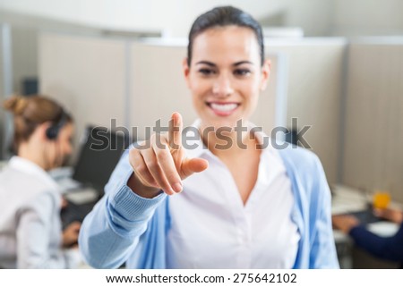 Smiling female customer service executive pointing at you while colleague working in background at call center