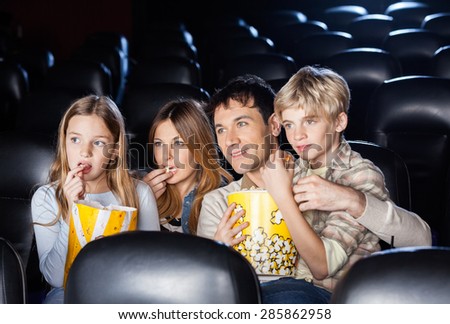 Family of four eating popcorn while watching film in movie theater