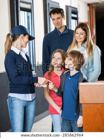 Female worker examining movie tickets of family at cinema