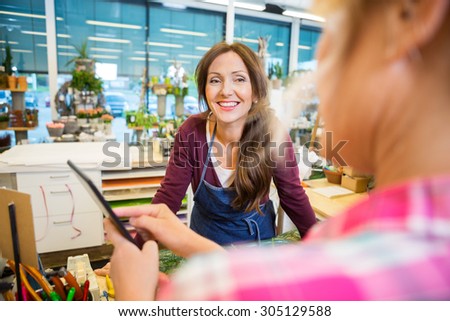 Happy florist looking at female customer using digital tablet in flower shop