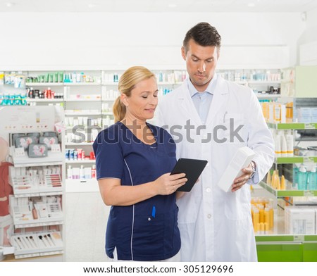 Female assistant using digital tablet while male pharmacist holding product in pharmacy