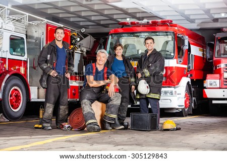 Portrait of happy firefighter\'s team with equipment against trucks at fire station