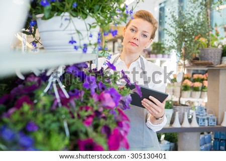 Portrait of mid adult florist holding digital tablet while standing by flower trolley in shop