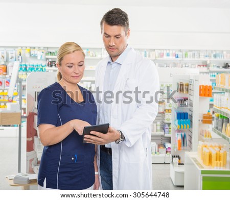 Female assistant using tablet computer with male pharmacist while standing in pharmacy