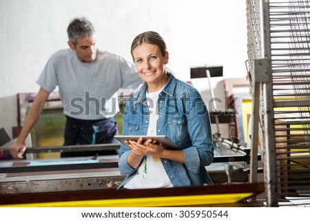 Portrait of smiling female worker holding digital tablet while colleague working in background at paper factory