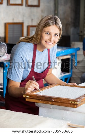 Portrait of mid adult female worker cleaning paper with tweezers in factory
