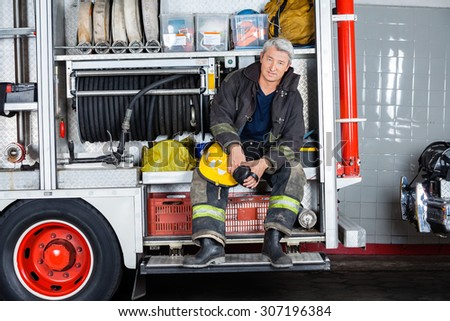 Full length portrait of confident fireman sitting in truck at fire station
