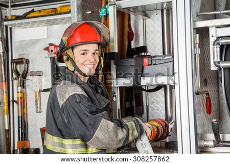 Portrait of happy male firefighter fixing water hose in truck at fire station