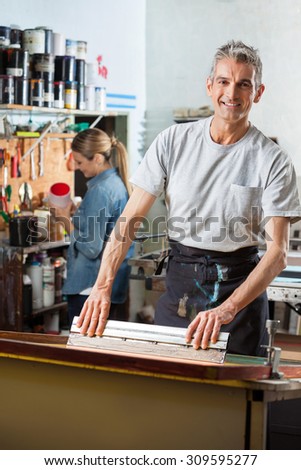 Portrait of confident mature worker using squeegee while female colleague working in background at factory