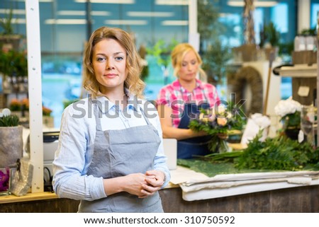 Portrait of confident female florist with colleague working in background at shop