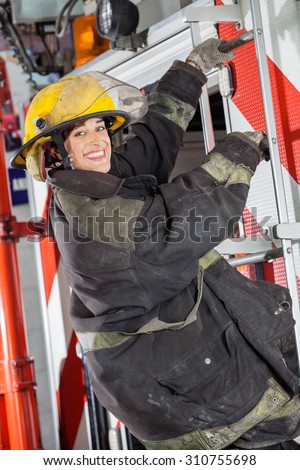 Side view portrait of happy firewoman standing on truck at fire station