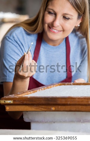 Smiling female worker removing large fibers from paper with tweezers in factory