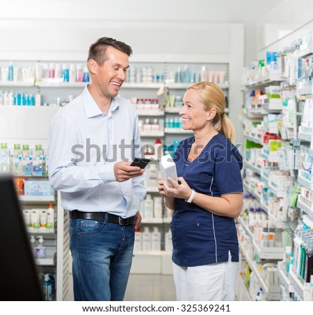 Happy mid adult male customer holding mobile phone while pharmacist showing product in pharmacy