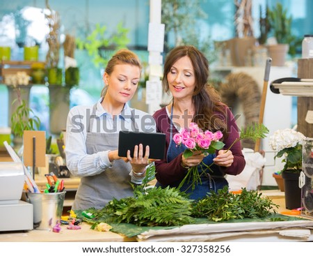 Florists using digital tablet while making bouquet of pink roses in flower shop