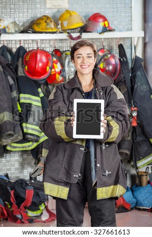 Portrait of confident firewoman showing digital tablet with blank screen at fire station