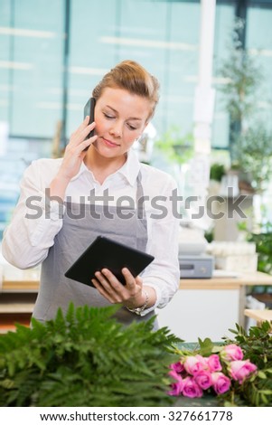 Female florist using mobile phone and digital tablet at counter in flower shop
