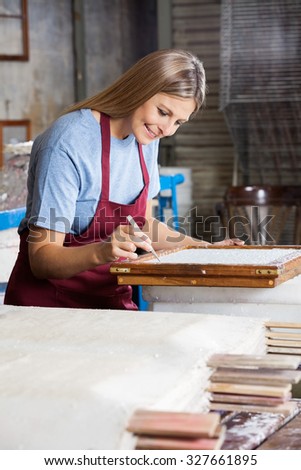 Smiling mid adult female worker cleaning paper using tweezers in factory