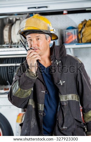 Mature fireman using walkie talkie while standing at fire station