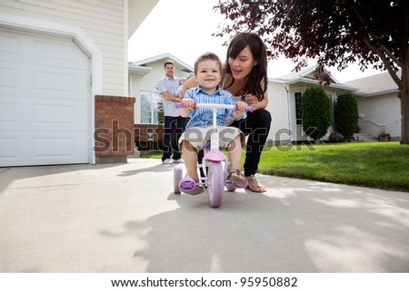 Beautiful happy young mother teaching her son to ride bike