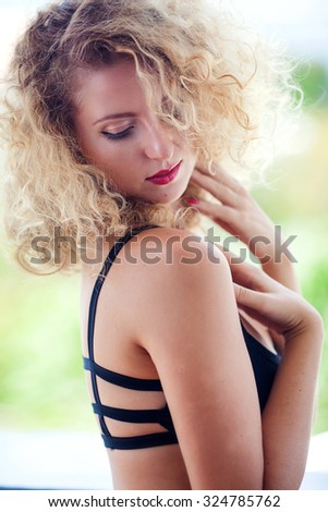 Portrait of young woman with blond curly hair, red lips and black eyeliner, hands with red nails, outdoors on sunny day