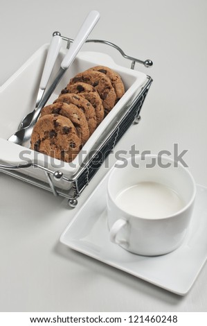 Top closeup view of biscuits in white ceramic plate with spoons and cup of milk on white wooden background