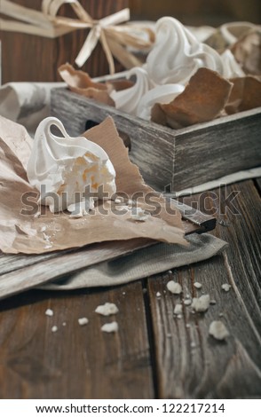 Closeup side view of half of meringue and crumbs on paper and wooden box with meringues on dark wooden background