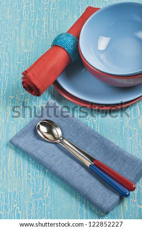 Top view of the kitchen utensils: red and blue plates, spoons and napkins on a blue cracked background