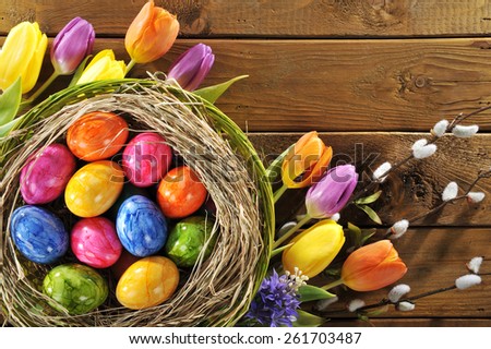 Easter nest with many colored henâ??s eggs, tulip, hyacinth and pussy willow on old wooden board