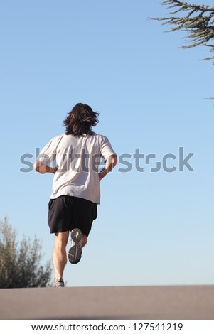 Back view of a man running on a road with the sky in the background