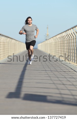 Front view of a sportsman running on a bridge with the blue sky in the background