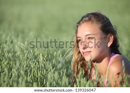 Portrait of a beautiful teenager girl face in an unfocused green oat meadow