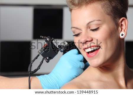 Beautiful woman looking how somebody is making a tattoo on her shoulder