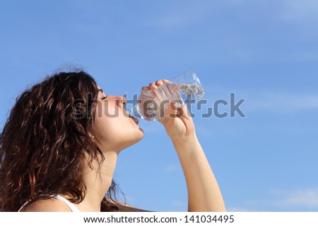 Profile of a woman drinking water from a plastic bottle with a blue sky in the background