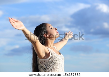 Beautiful arab woman breathing fresh air with raised arms with a cloudy blue sky in the background