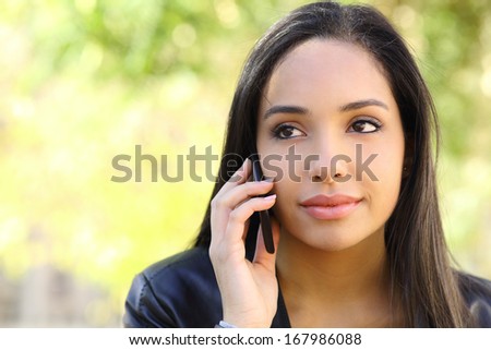 Portrait of a beautiful woman on the mobile phone in a park with a green unfocused background
