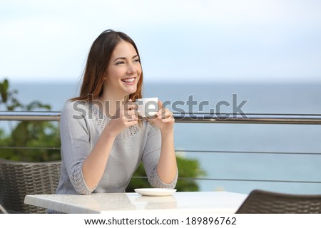 Beautiful woman holding a cup of coffee in a restaurant with the sea in the background