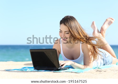 Happy teenager girl browsing social media in a laptop on the beach witj the sea in the background