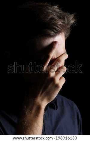 Worried or embarrassed man covering his face with hand isolated on a black background