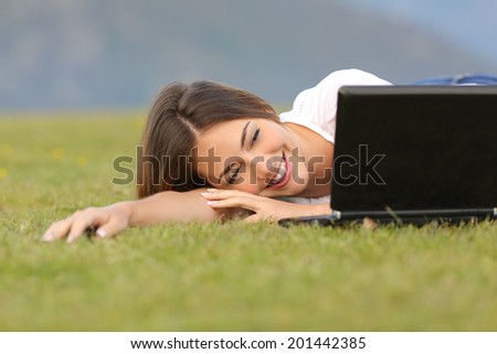 Happy woman watching videos in a laptop lying on the grass with a green unfocused background