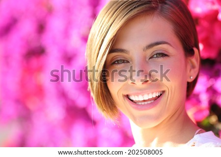 Beautiful woman smiling with white perfect teeth with a warmth lot of pink flowers in the background