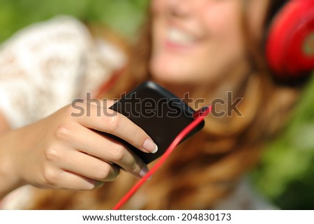 Woman hand using a smart phone to listen to the music with headphones with a green background