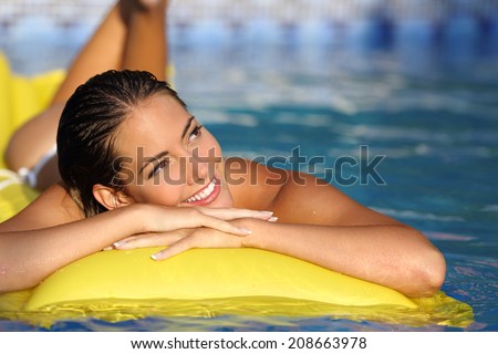 Happy girl enjoying summer vacations on a mattress in a pool and looking at side while thinking