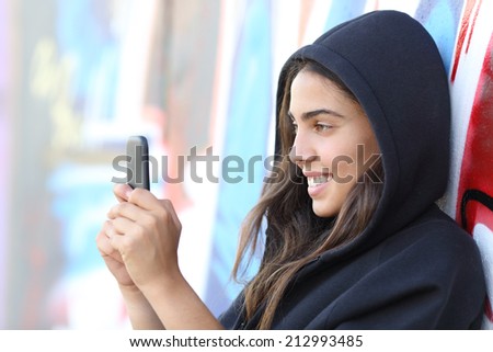 Skater style teen girl reading happy her smart phone with an unfocused graffiti wall in the background